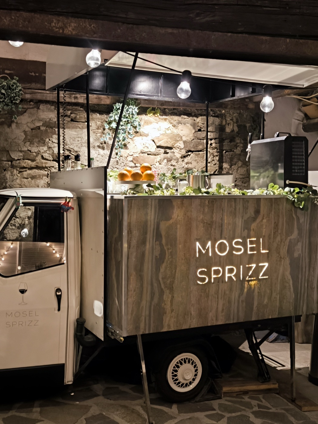 Die Holzbar der Ape mit leuchtendem Mosel-Sprizz-Schriftzug am Abend